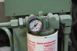 Cette photo représente un système de filtration basse pression sur le retour d’une unité hydraulique dont le manomètre différentiel est hors d’usage. Considérant le contexte opérationnel de l’équipement, le remplacement annuel de la cartouche filtrante est recommandé. Malgré cela, on doit effectuer une vérification visuelle mensuelle de l’aiguille du manomètre différentiel afin de déceler une problématique potentielle entre les changements de filtre. Comme le manomètre est hors d’usage, il est impossible d’effectuer cette importante vérification. Rappelons qu’un manomètre différentiel nous permet de visualiser le degré de colmatage de l’élément filtrant et que des inspections visuelles régulières permettent de vérifier la vitesse à laquelle le colmatage s’effectue. 